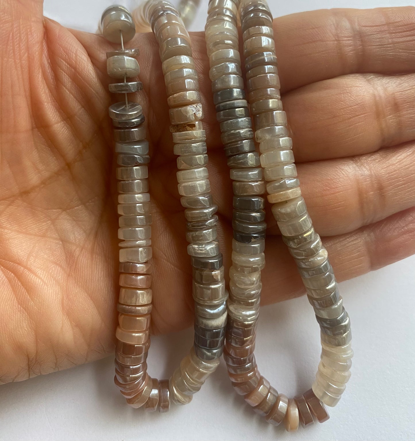 A person holding a smooth wheeel moonstone gemstone strand, showcasing its brown-golden facets and elegant design.