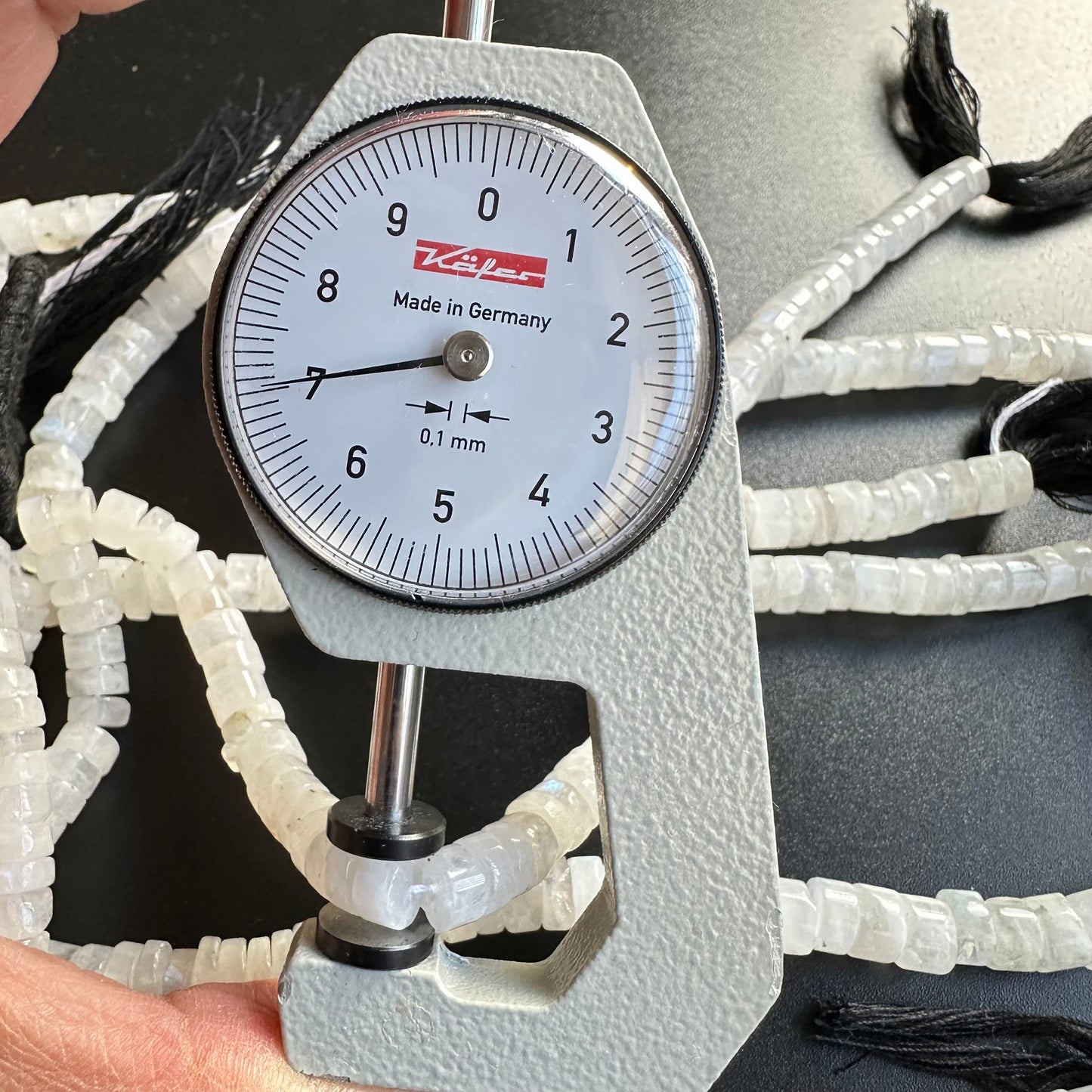 A dial gauge measures the Moonstone smooth wheel gemstone beads, ensuring precise 7.0-7.1mm sizing.