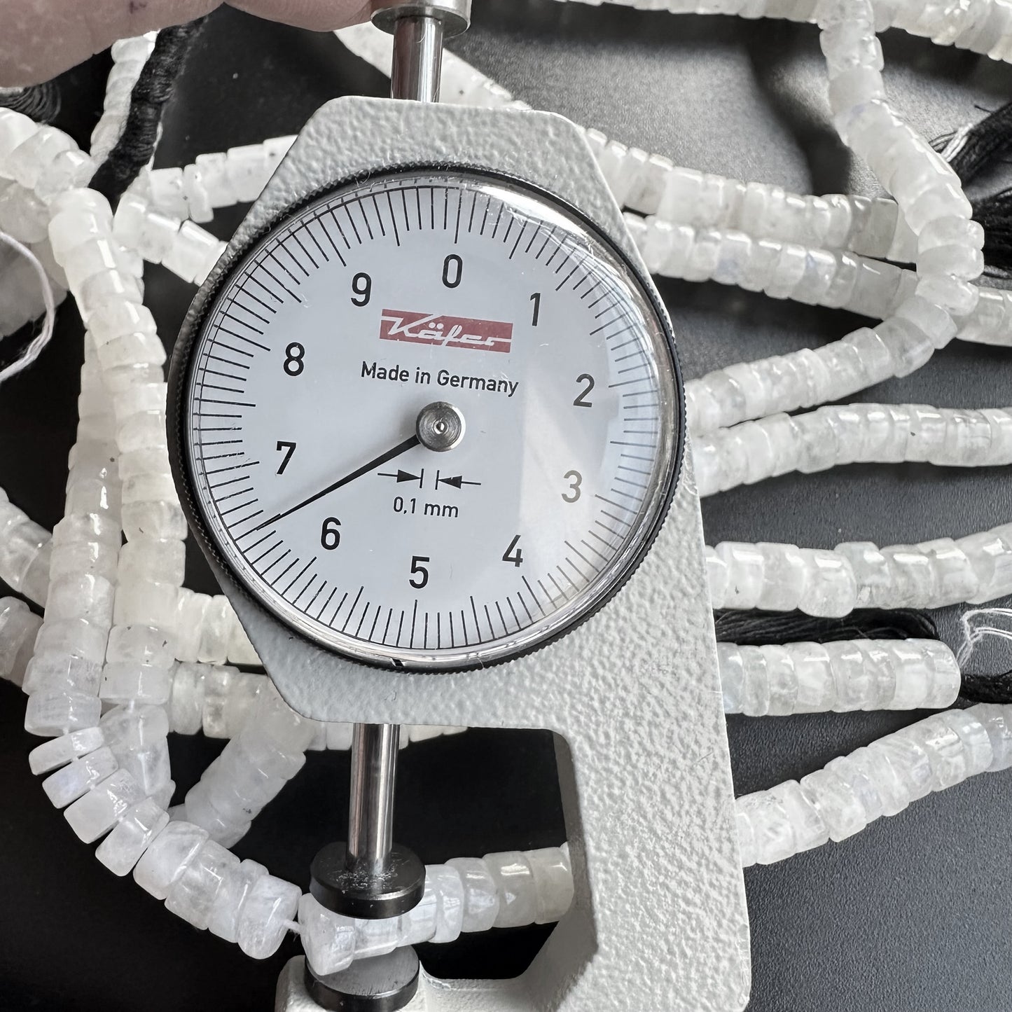 A dial gauge measures the Moonstone smooth wheel gemstone beads, ensuring precise 7.0-7.1mm sizing.
