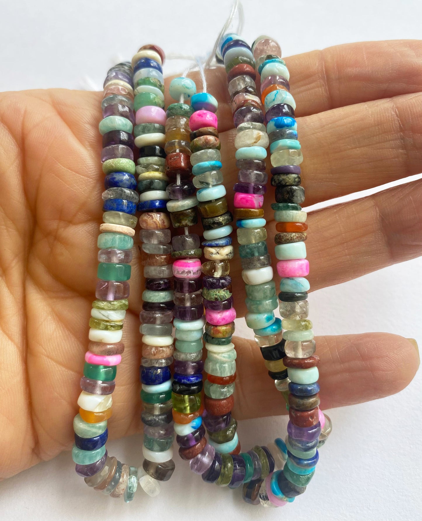 A person holds delicate strands of Multi Disco beads, showcasing their smooth design.