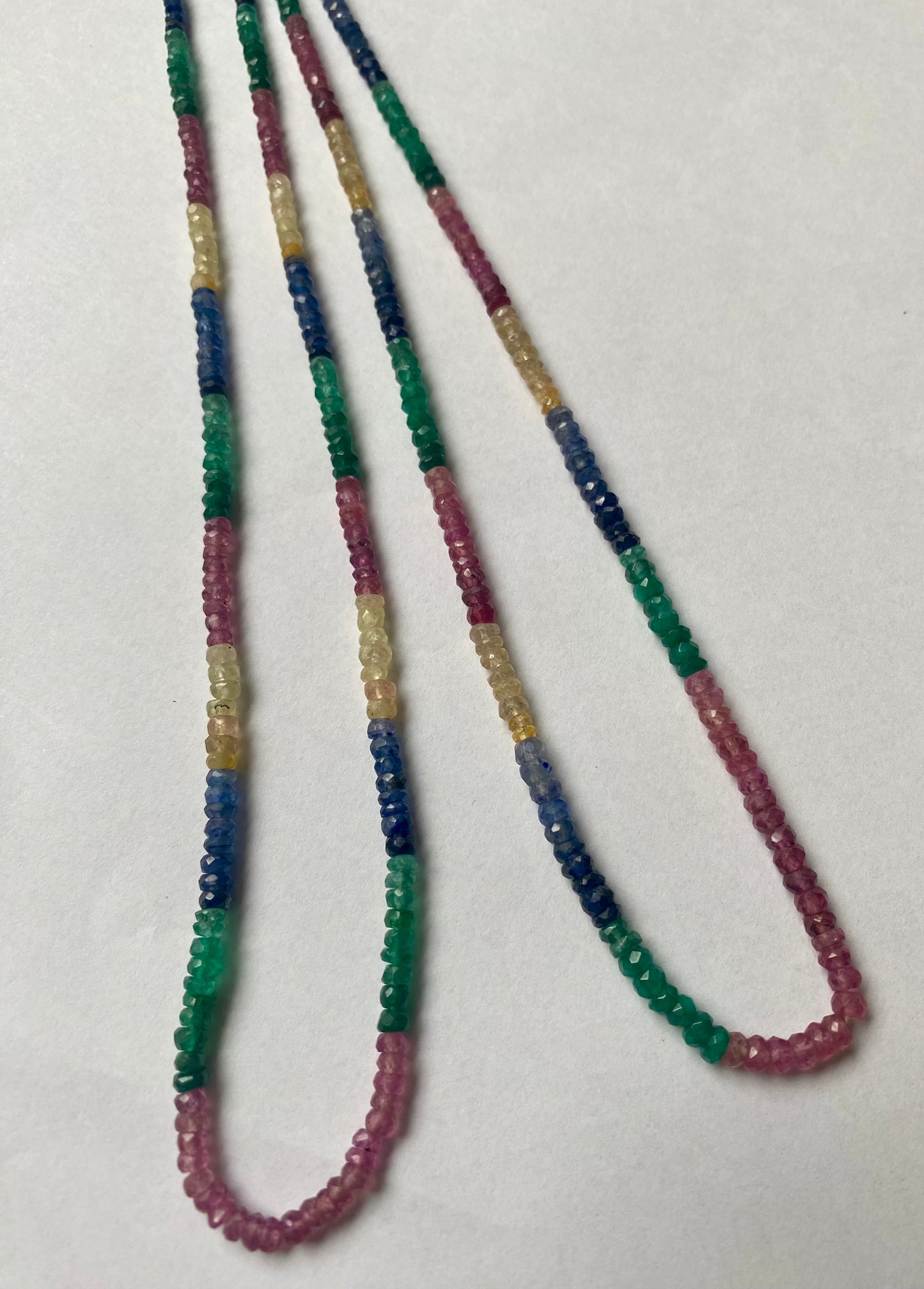 Striking strands with multi-coloured beads, including ruby, blue sapphire, yellow sapphire, and emerald, set on a white background.