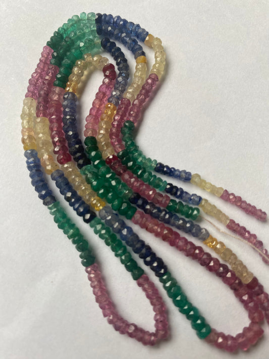 A colourful strand made of faceted rondelle beads in ruby, blue sapphire, yellow sapphire, and emerald against a white backdrop.