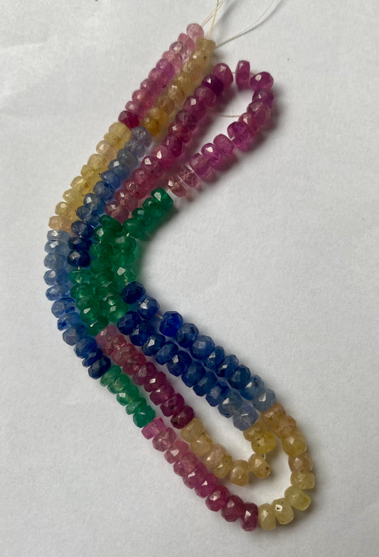 A colourful strand made of faceted rondelle beads in ruby, blue sapphire, yellow sapphire, and emerald against a white backdrop.