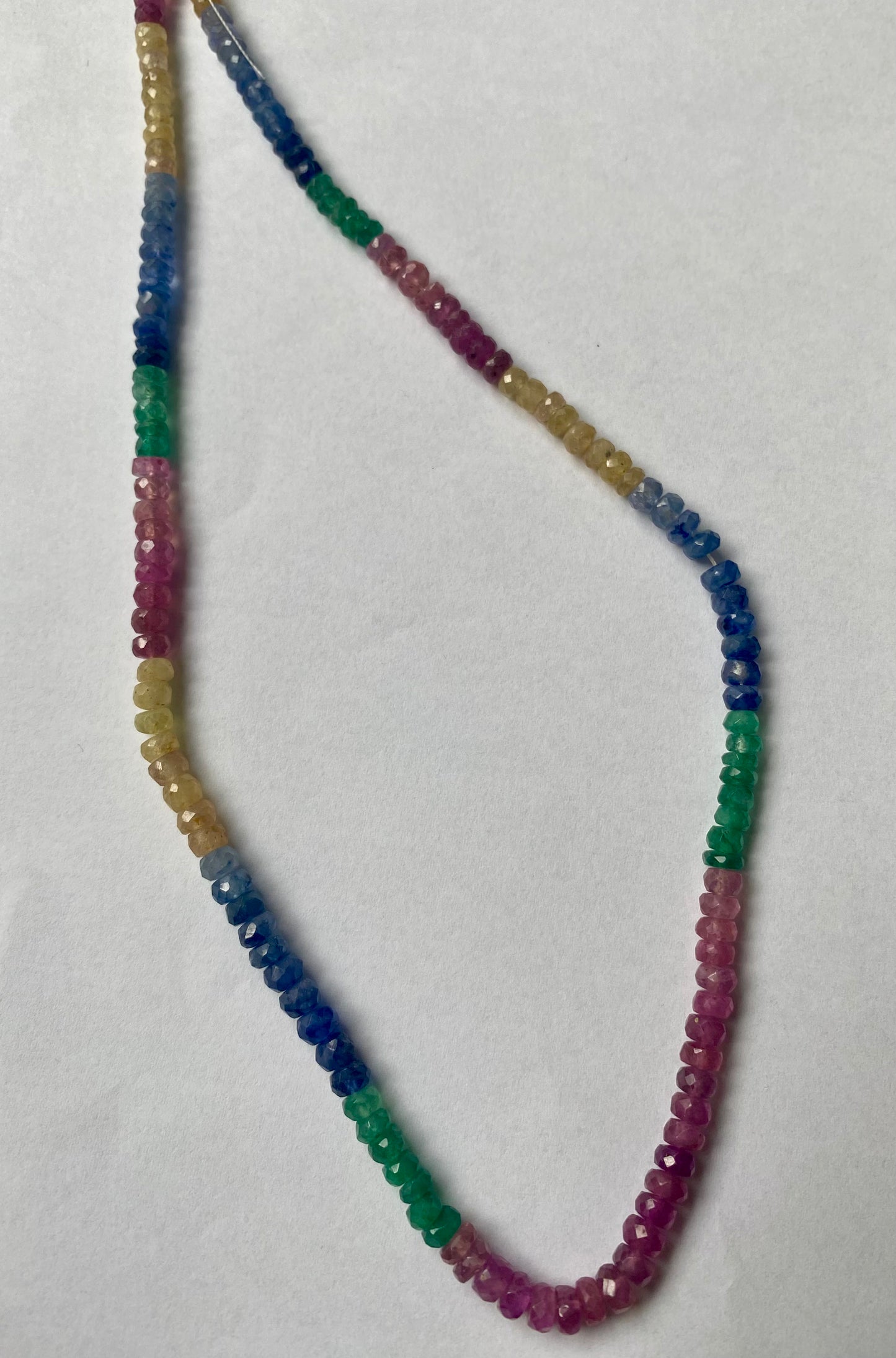 A striking strand with multi-coloured beads, including ruby, blue sapphire, yellow sapphire, and emerald, set on a white background.