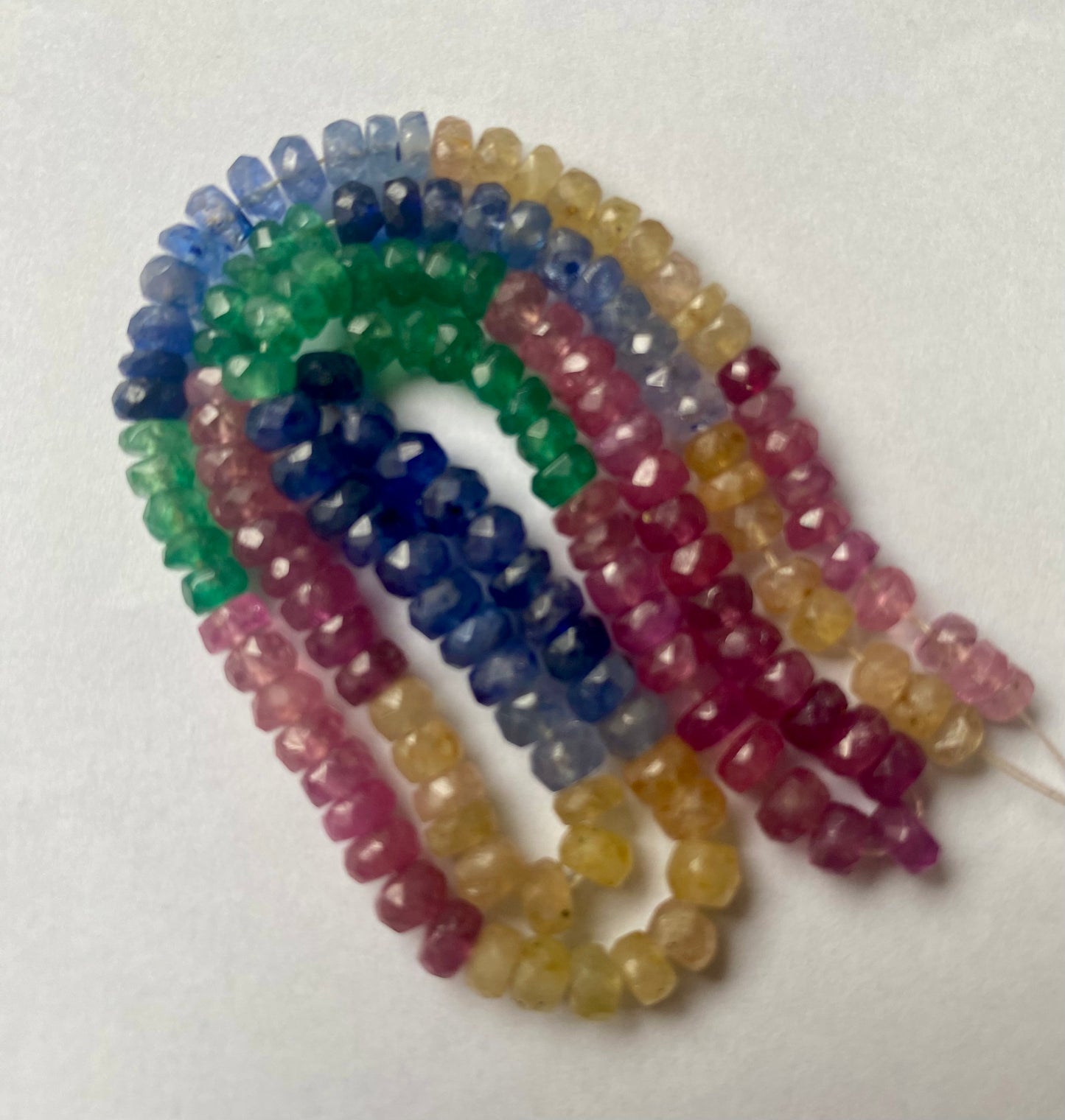 A vibrant multi-coloured strand featuring ruby, blue sapphire, yellow sapphire, and emerald beads 4mm to 5mm on a white background.