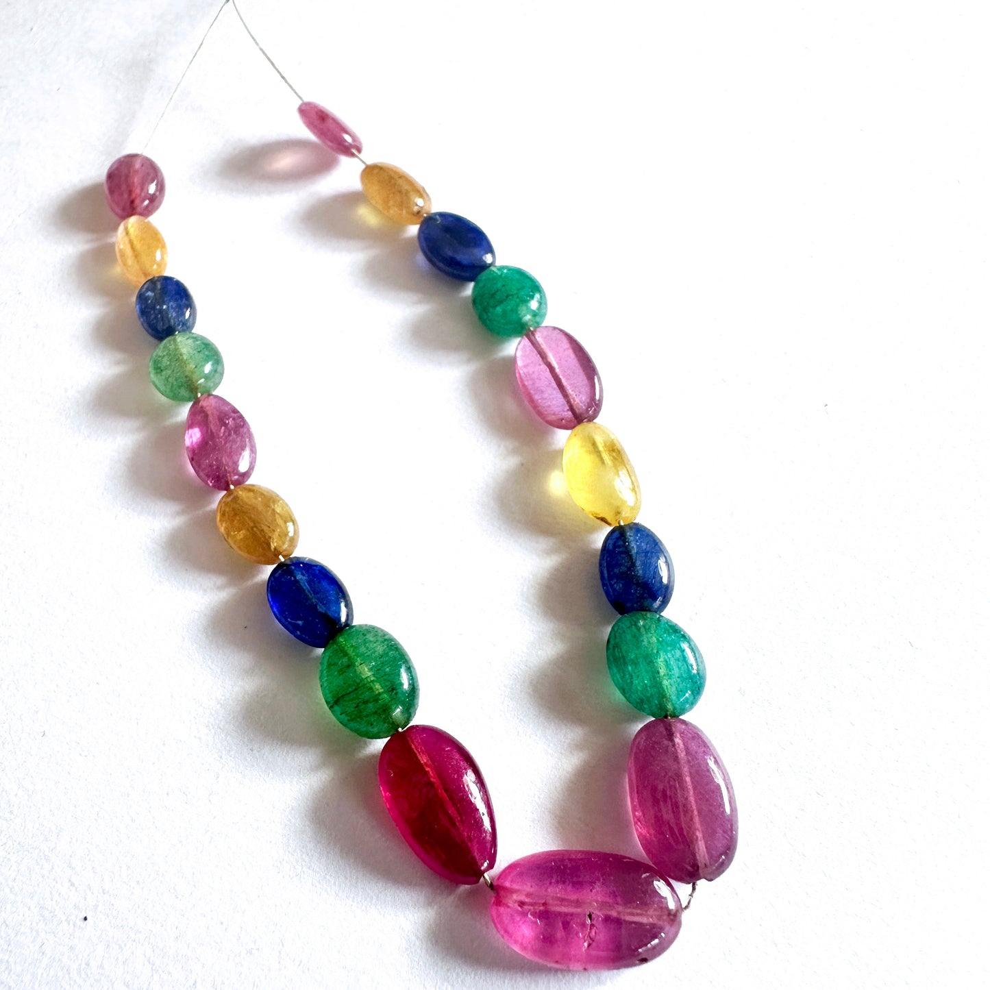 Ruby, emerald, and sapphire oval beads display vivid colour and high-quality polish in a balanced arrangement.