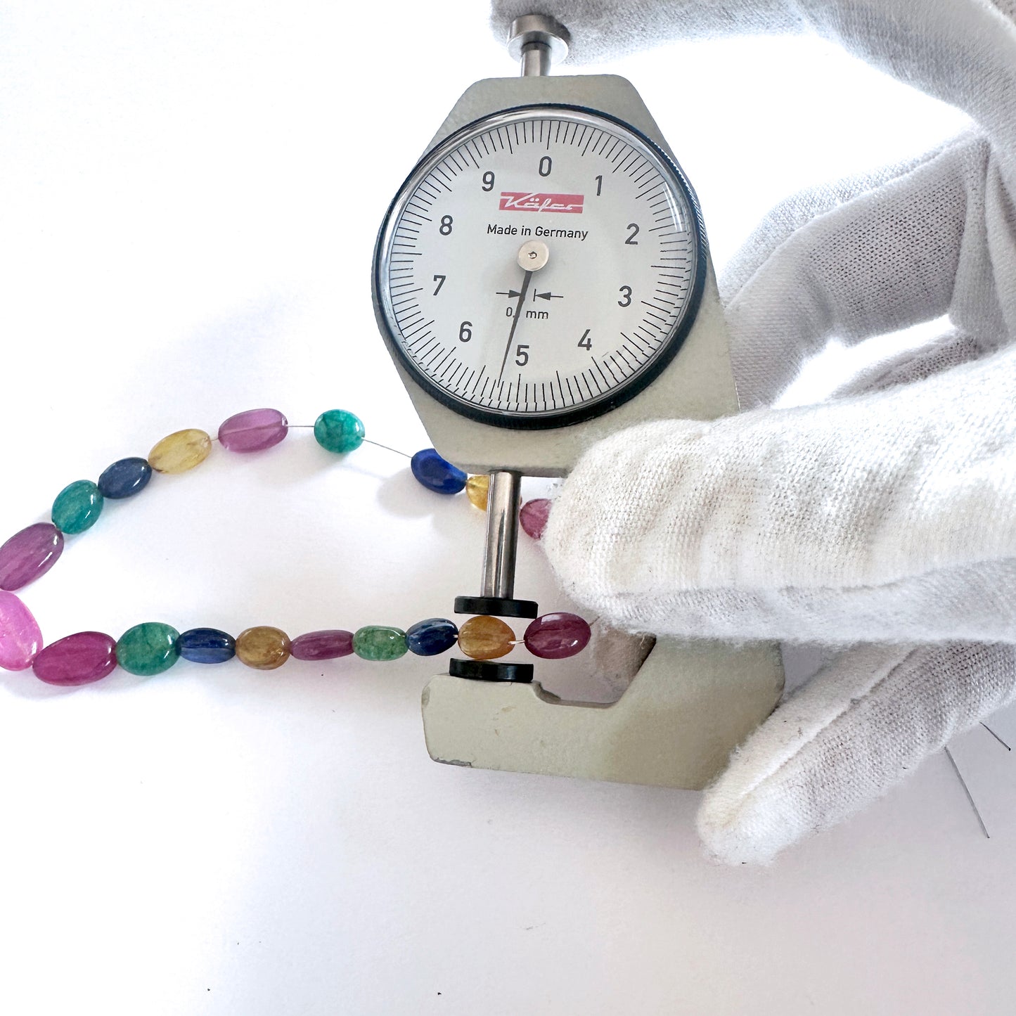 A dial gauge measures the blue sapphire smooth oval gemstone for precision and quality.