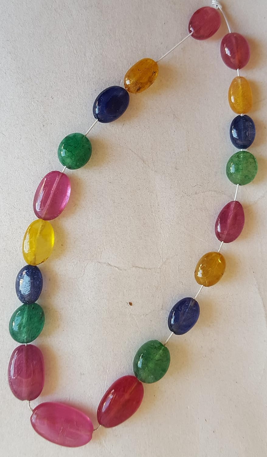 A vibrant multi-coloured strand featuring ruby, blue sapphire, yellow sapphire, and emerald beads on a white background.