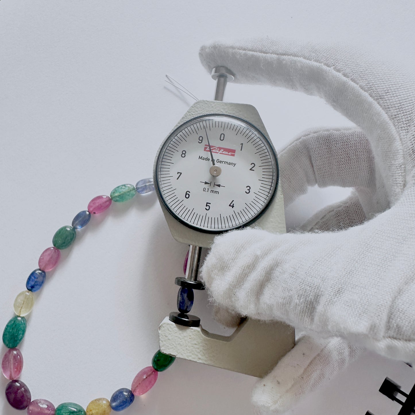 A dial gauge measures the emerald smooth oval gemstone for precision and quality control.