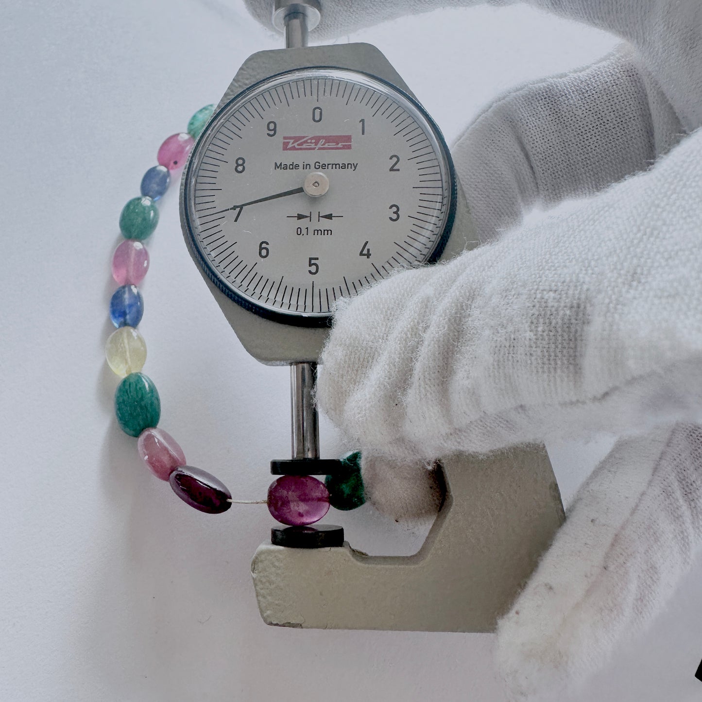 A dial gauge measures the emerald smooth oval gemstone for precision and quality control.