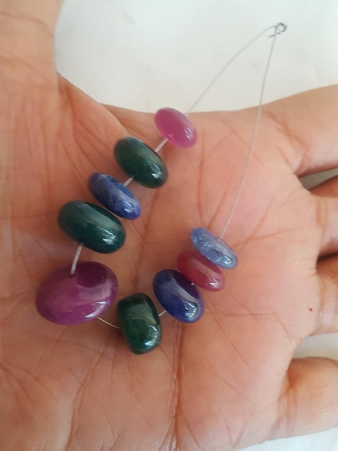 A person holds a vibrant bunch of multi-coloured smooth beads, including ruby, blue sapphire, and emerald.