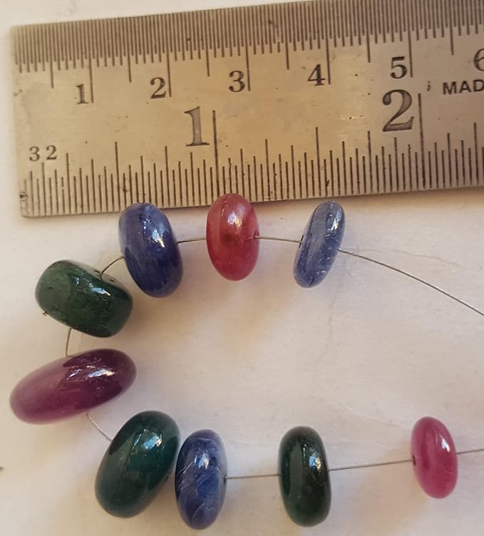 Close-up of a ruler beside colourful multi-precious beads, including ruby, blue sapphire, and emerald.