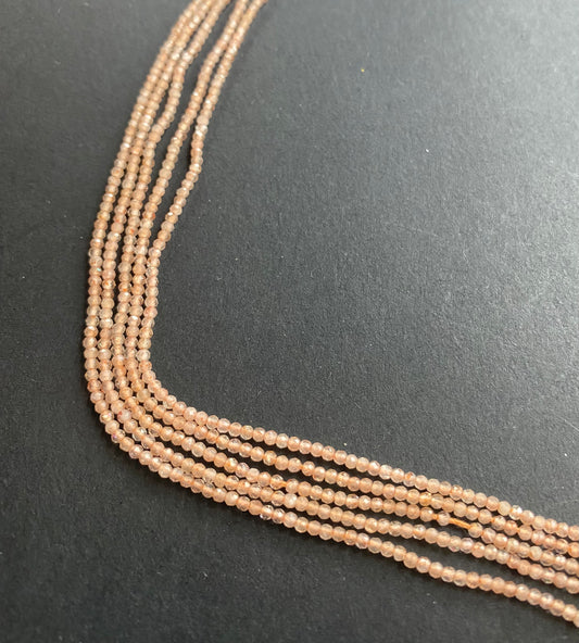 Strand of peach-coloured micro-faceted beads is displayed on a black surface, creating a striking contrast and visual appeal.