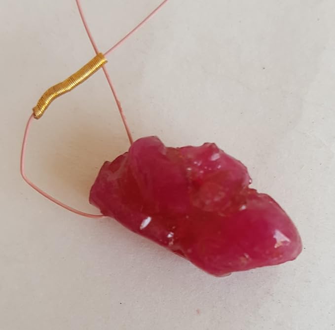A stunning 17-carat red ruby drilled rough, elegantly hung from a delicate red tassel.