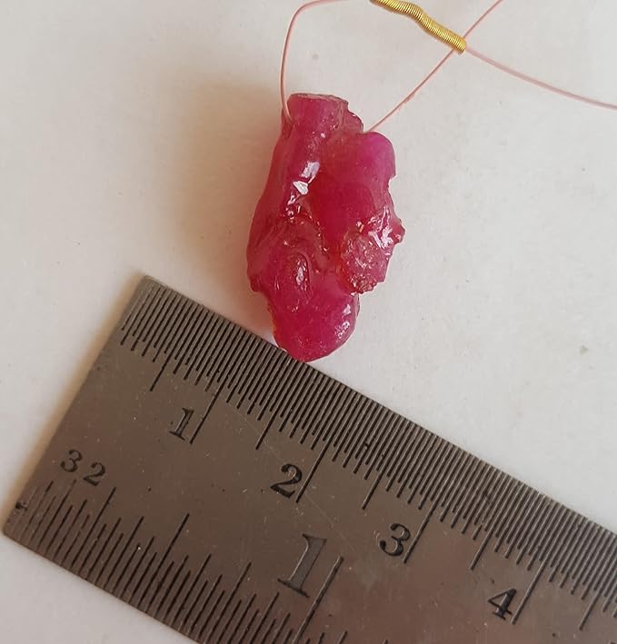 Close-up of a measuring ruler beside colourful precious ruby bead.
