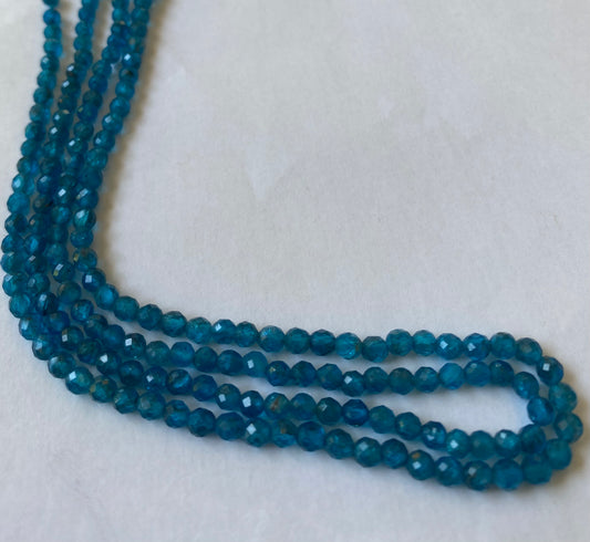 Close-up of a blue gemstone bead strand highlighting neon apatite faceted rondelle gemstones.