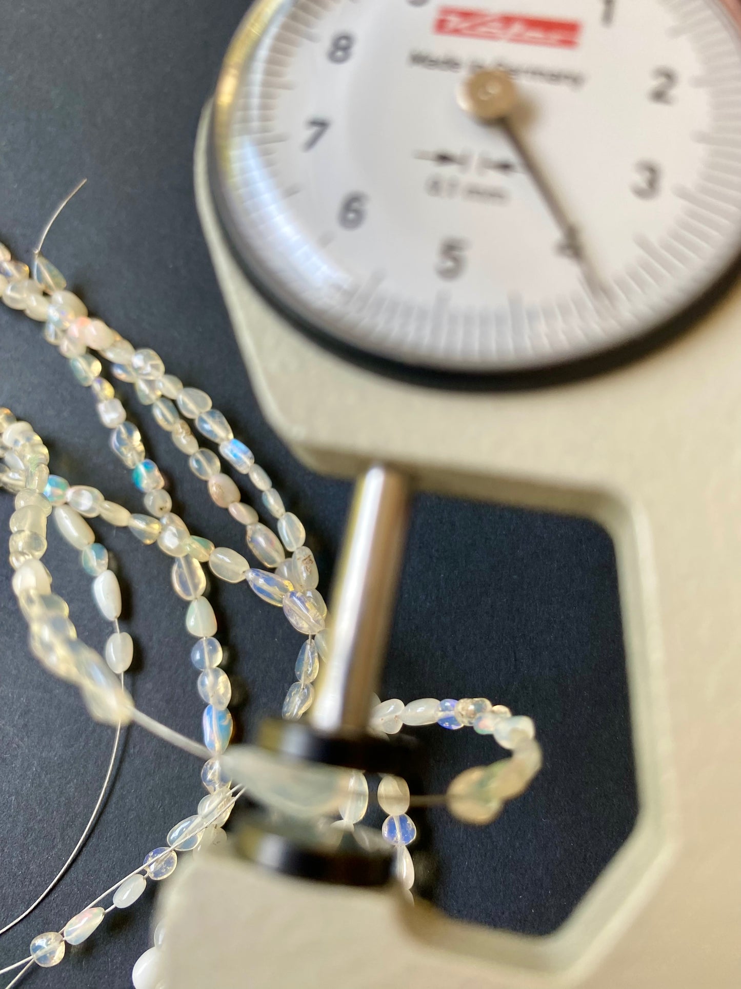Close-up of a measuring dial gauge tool alongside a string, highlighting the precision of measurements for Opal Beads.