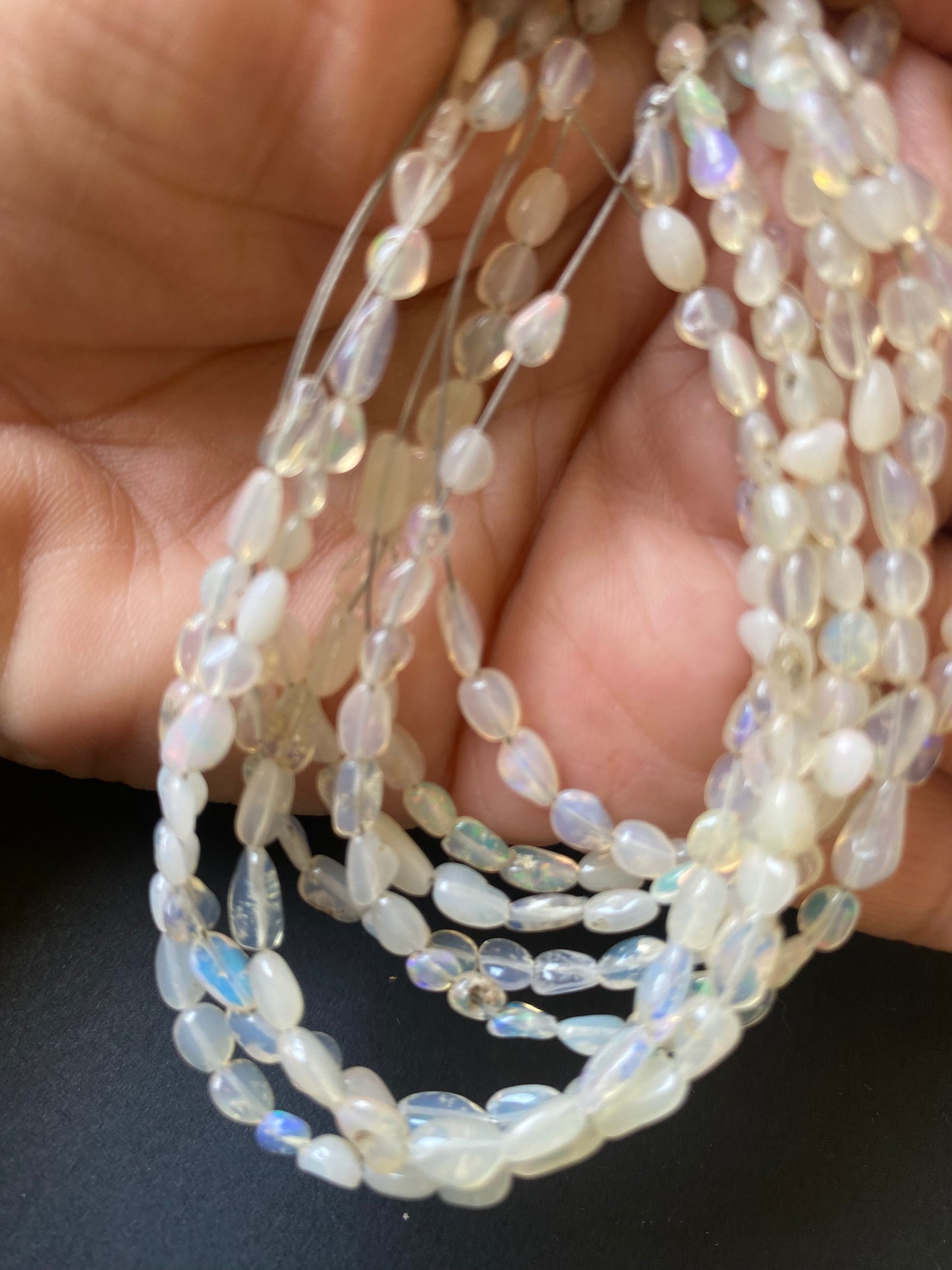A person holding a smooth strand of Opal beads, showcasing their elegant white colour and fire.
