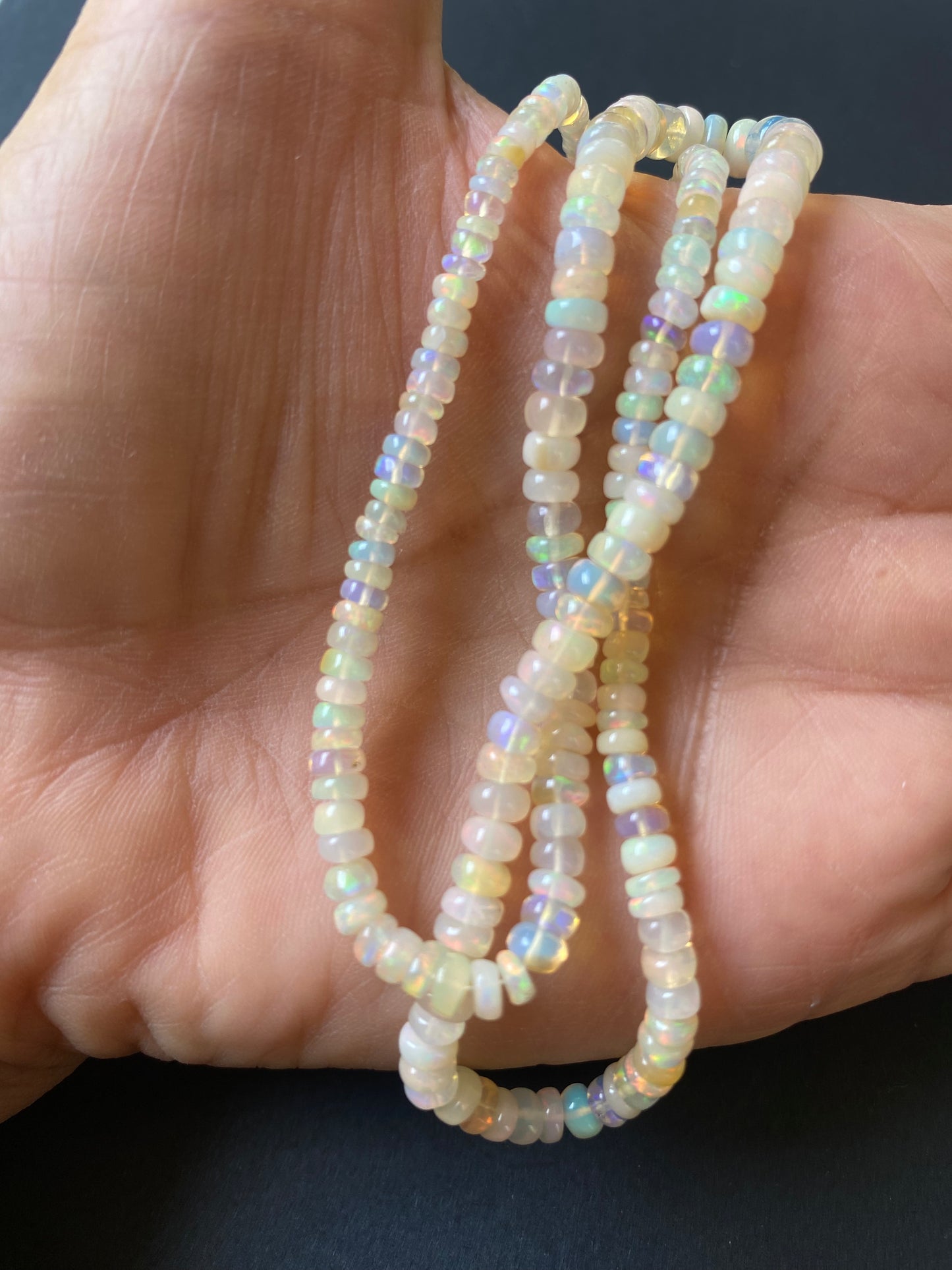Close-up of a person grasping a strand of smooth rondelle Opal beads, each 2.7mm-5mm in size, highlighting their beauty.