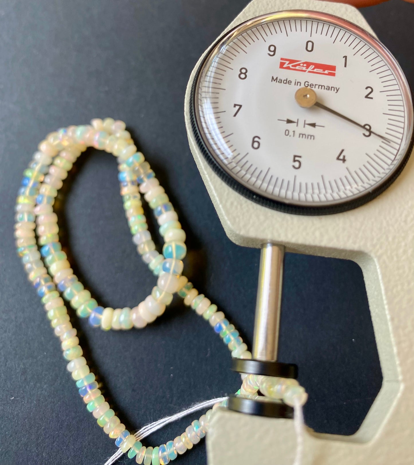Close-up of a measuring dial gauge tool alongside a string, highlighting the precision of measurements for Opal jewellery.