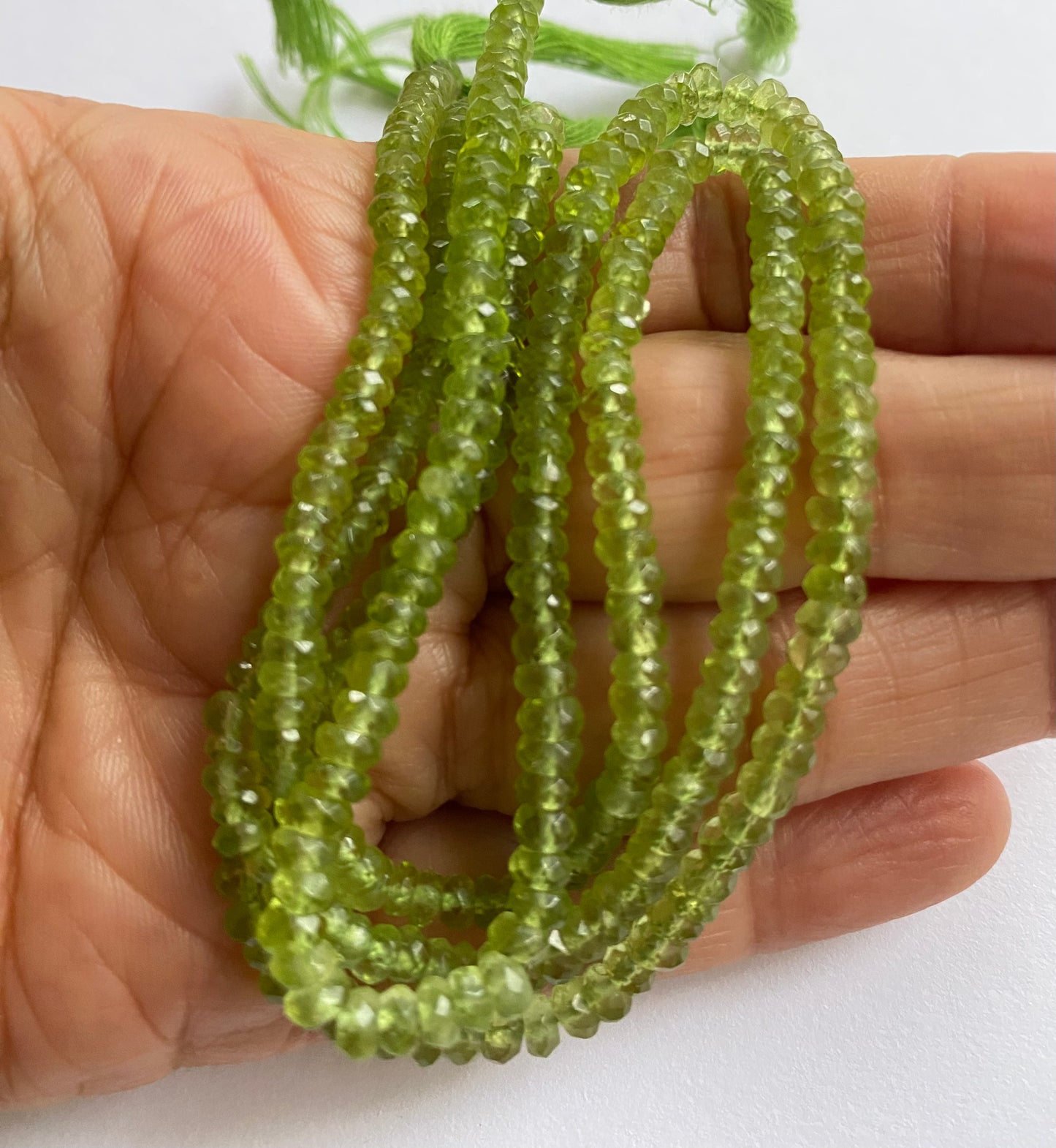 A person holding a strands of faceted green peridot rondelle precious gemstone beads, showcasing their vibrant colour and shine.