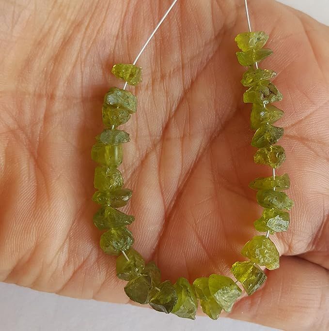 A hand holding a cluster of green peridot gemstone beads, showcasing their rough texture and vibrant colour.