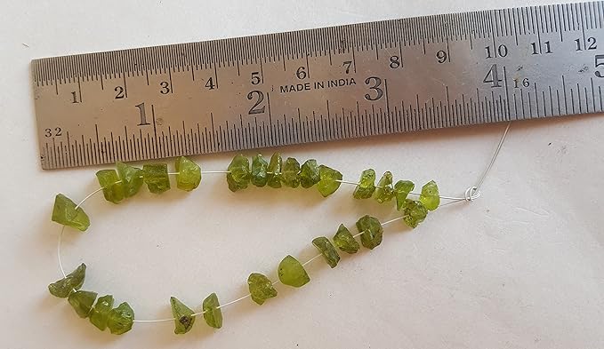 A ruler placed next to a group of green peridot beads, each measuring between 7mm and 8.5mm.