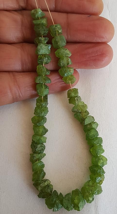A person holding a strand of rough green peridot beads, showcasing the colour and natural shape.