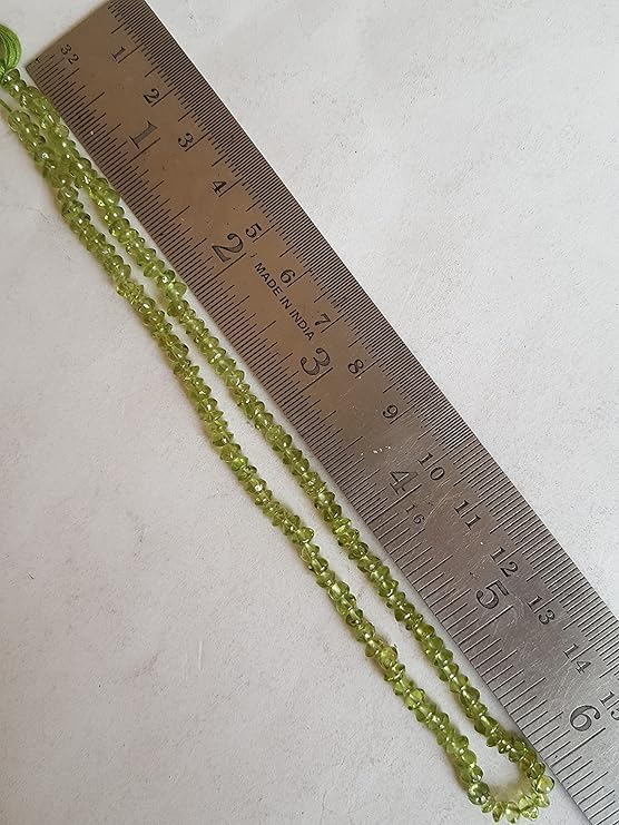 Close-up of a measuring ruler alongside green peridot beads, showcasing their faceted rondelle shape and size.