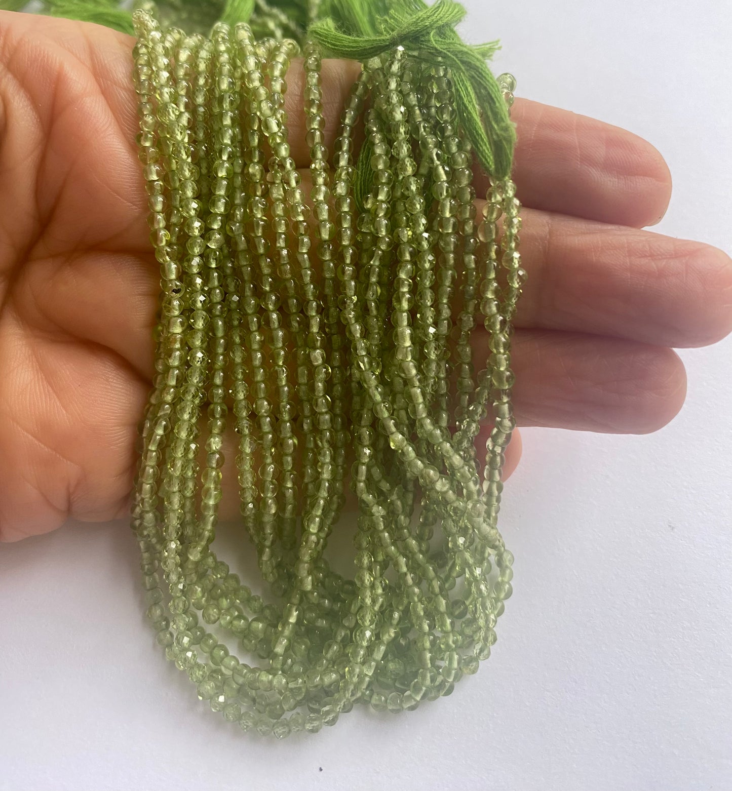 A person holding a smooth rondelle peridot gemstone strand, showcasing its green facets and elegant design.