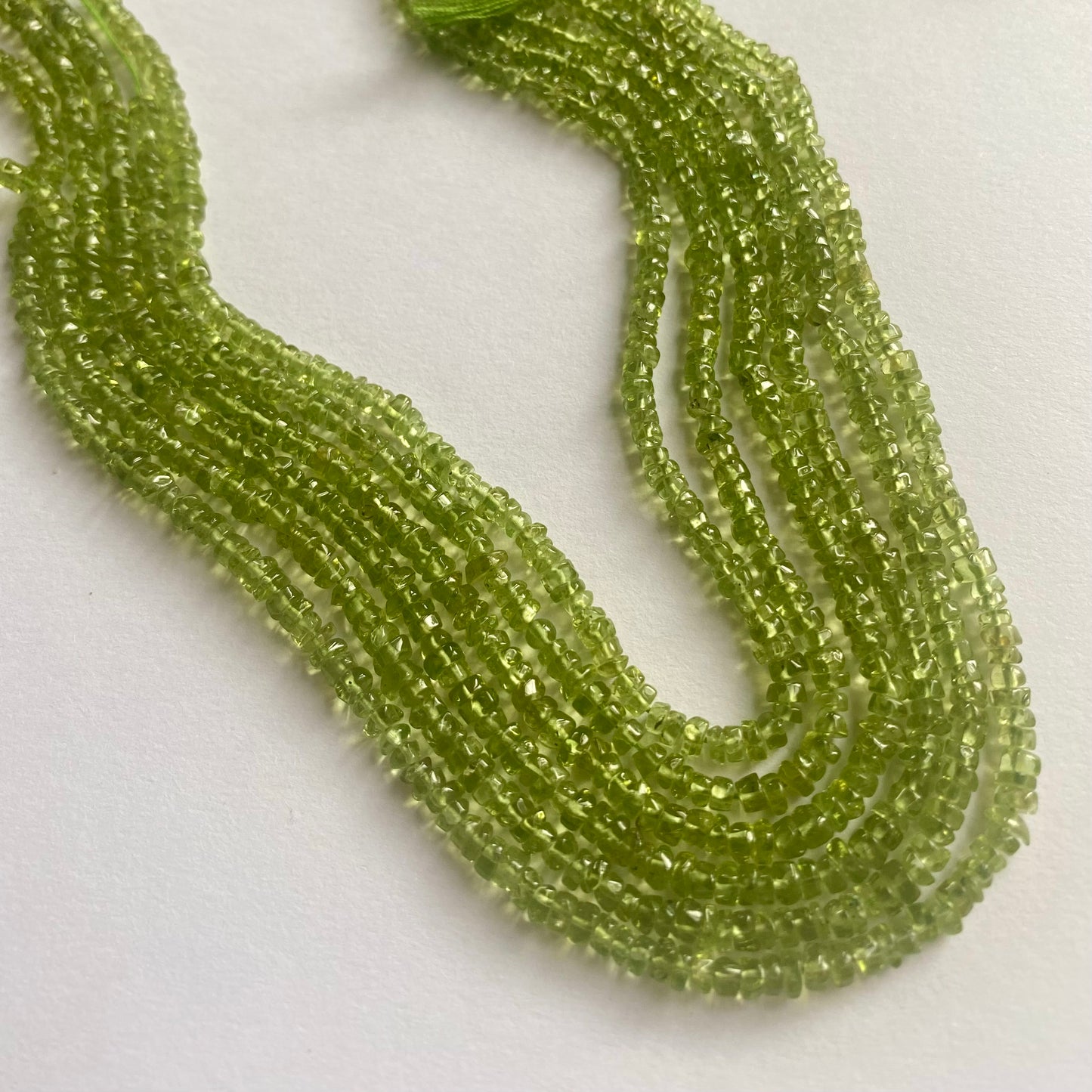 Strands of polished green peridot beads, 3.5mm to 4mm, displaying a bright and eye-catching green colour.