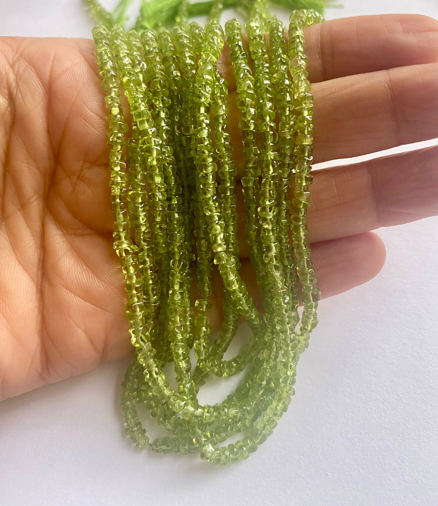 A person holding a strand of smooth green peridot beads, showcasing their vibrant colour and round shape.