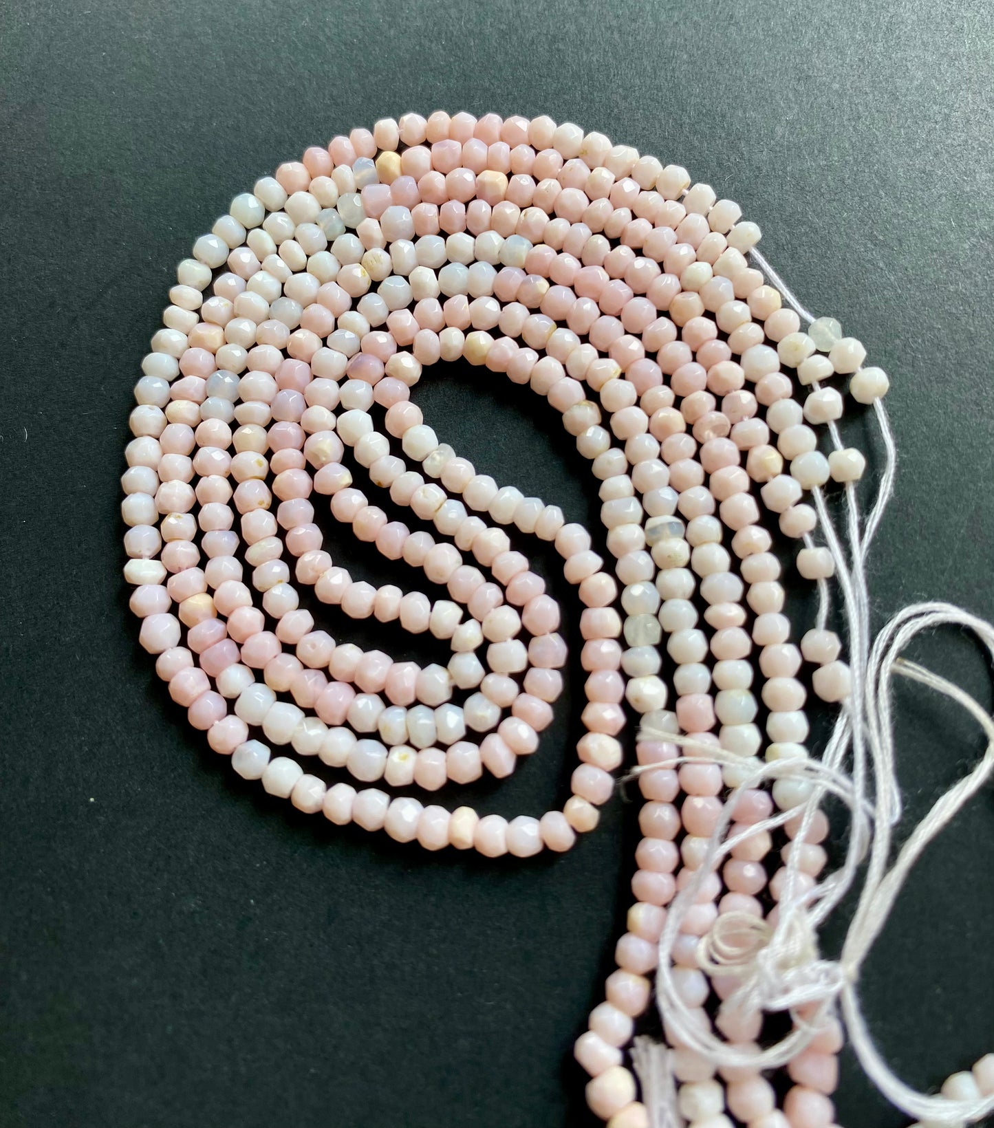 A close-up of a strand of Pink Opal gemstone beads, faceted rondelles ranging from 3.5mm-4mm, glistening in the light.