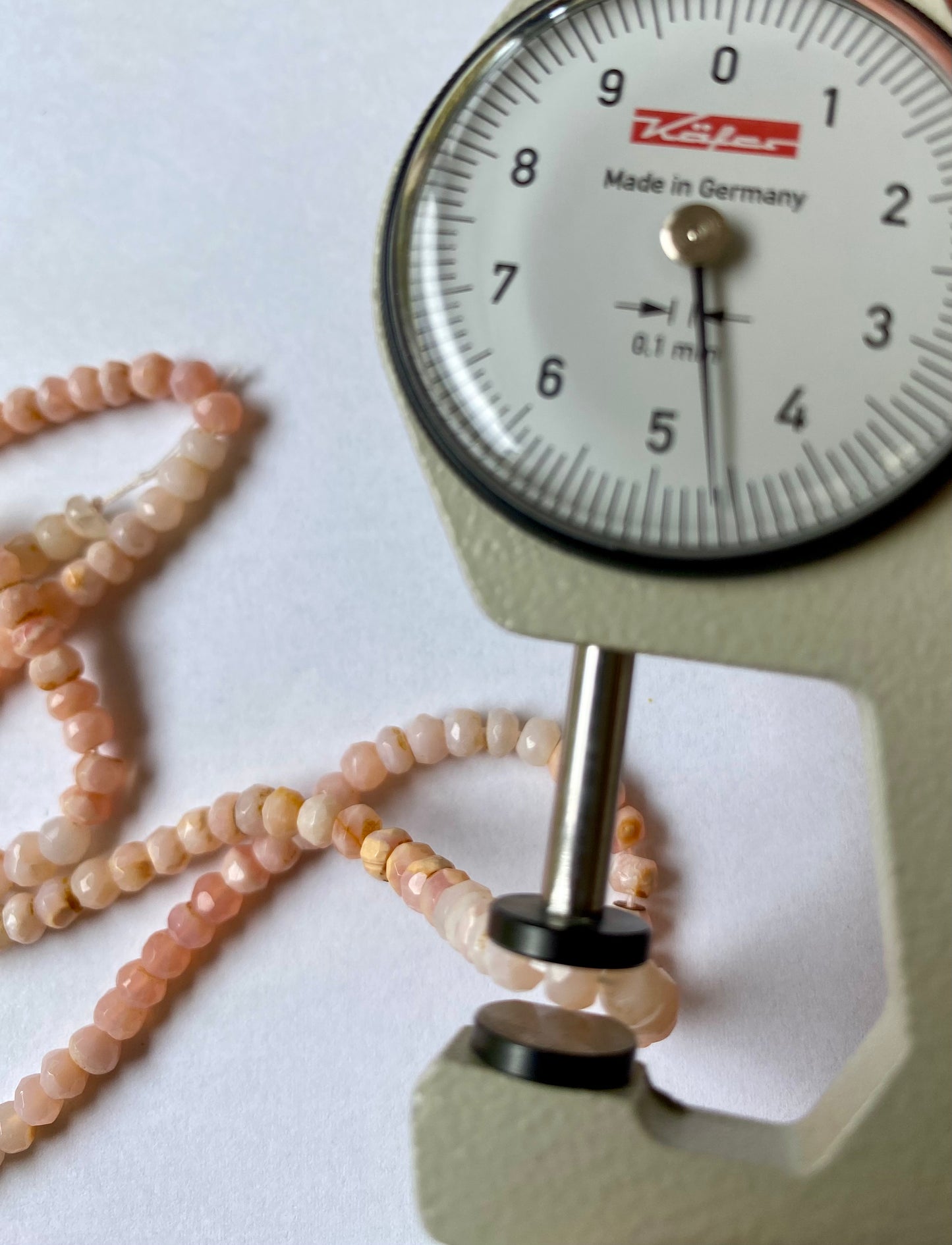 Close-up of a measuring dial gauge tool alongside a string, highlighting the precision of measurements for Peruvian Opal jewellery.