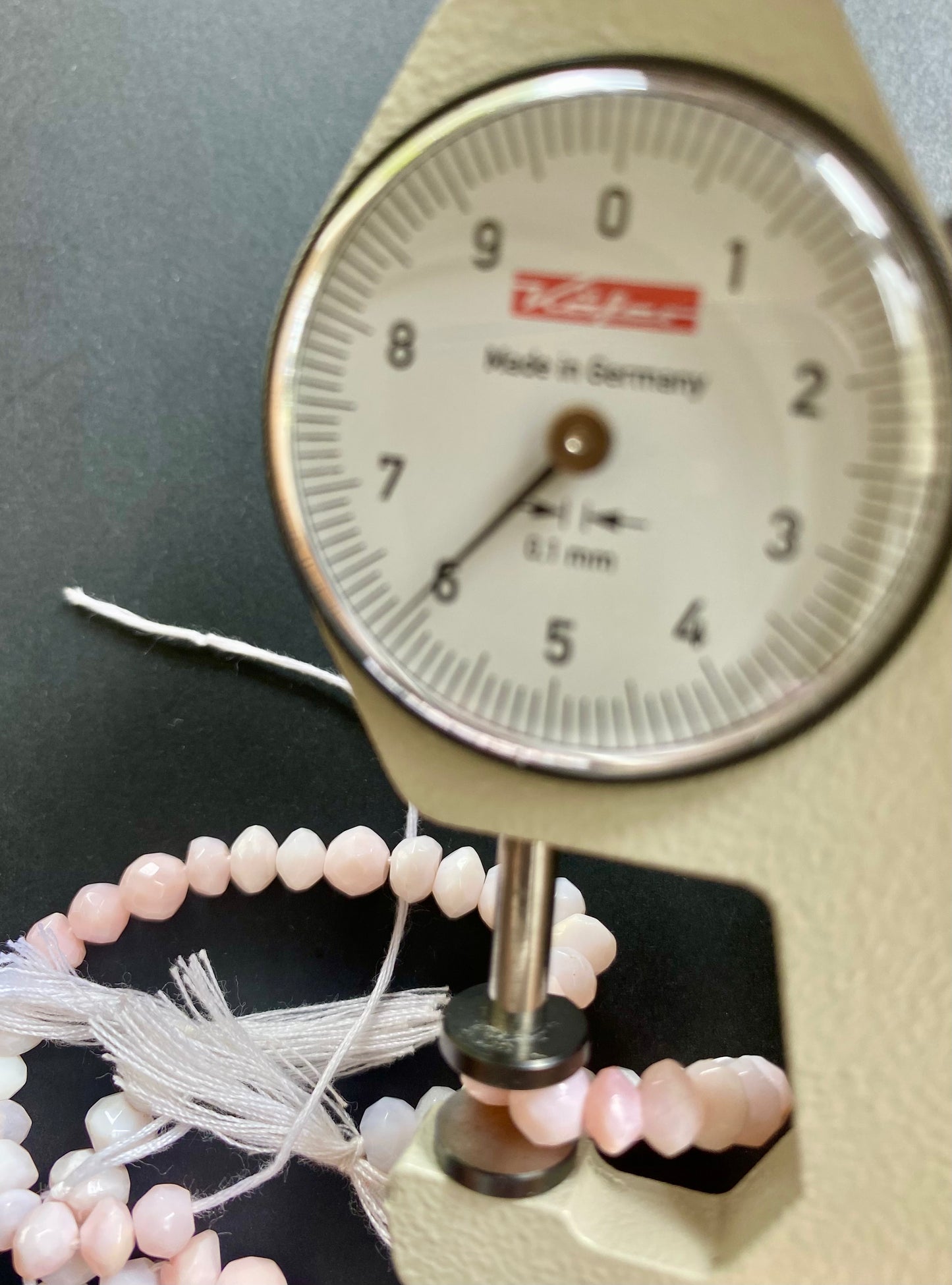 A person measuring a pink faceted rondelle bead with a dial gauge measure, showcasing its size and detail.