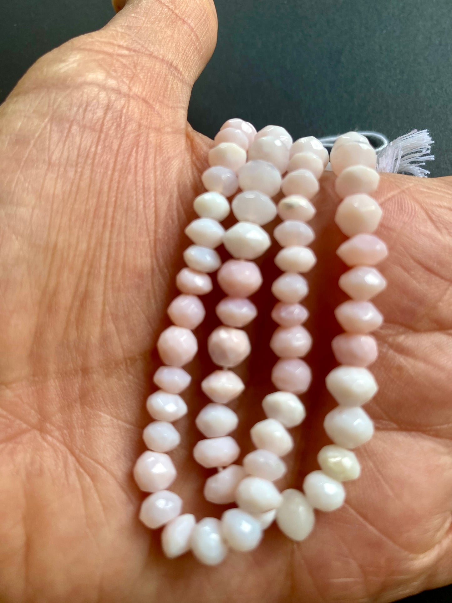 A person holding a strands of faceted rondelle semi precious gemstone opal beads, showcasing their vibrant colour and shine.