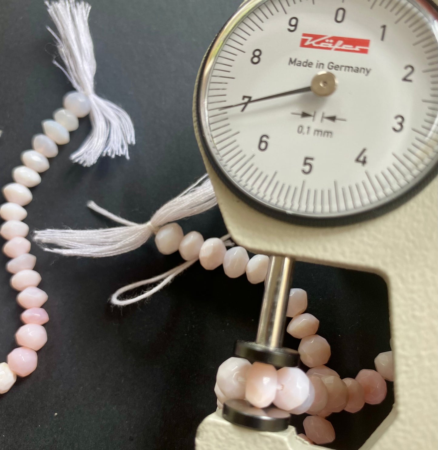 A person measuring a pink faceted rondelle bead with a dial gauge measure, showcasing its size and detail.