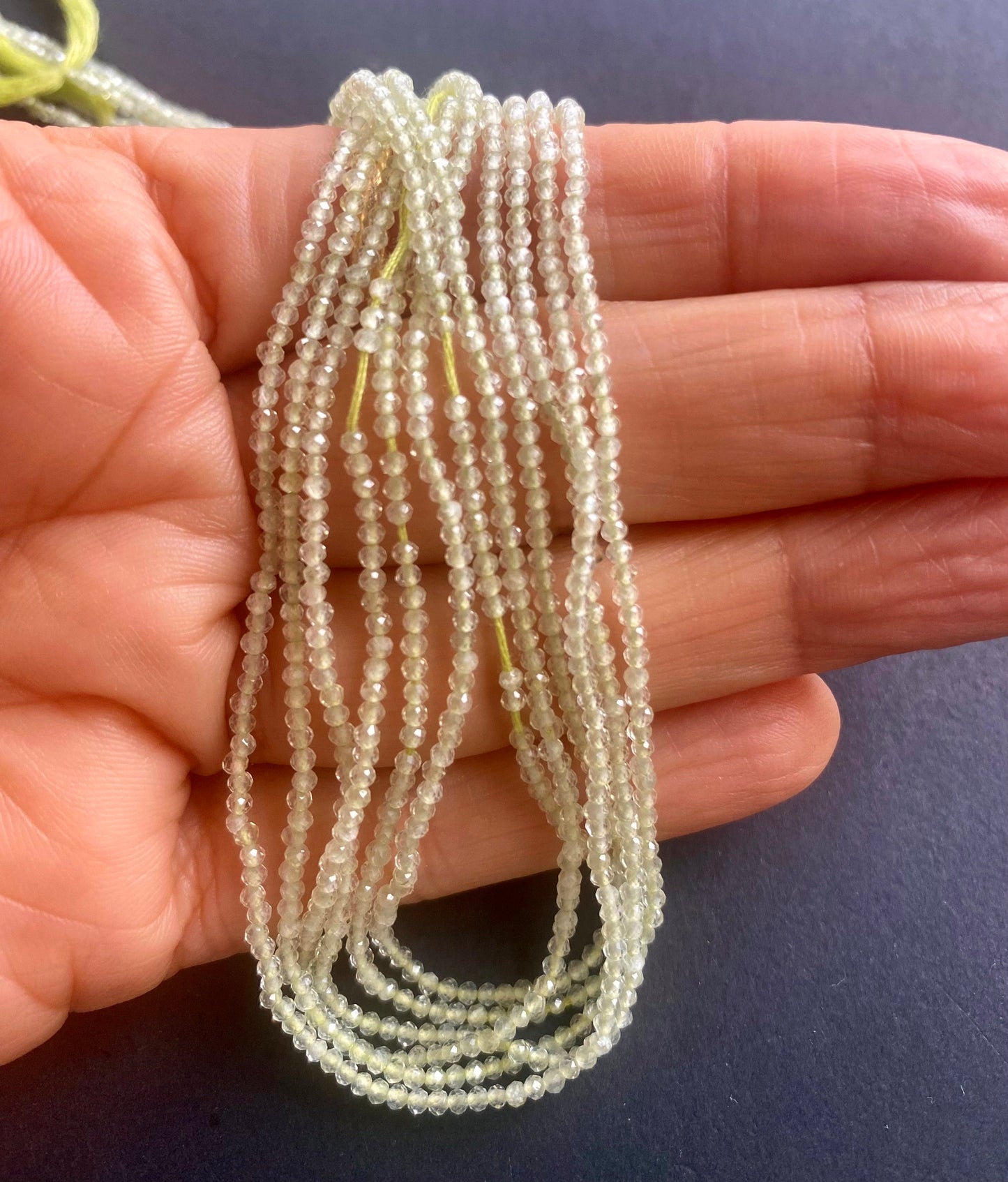 A hand holding a cluster of micro faceted natural prehnite stone beads, measuring 1.9mm in size.