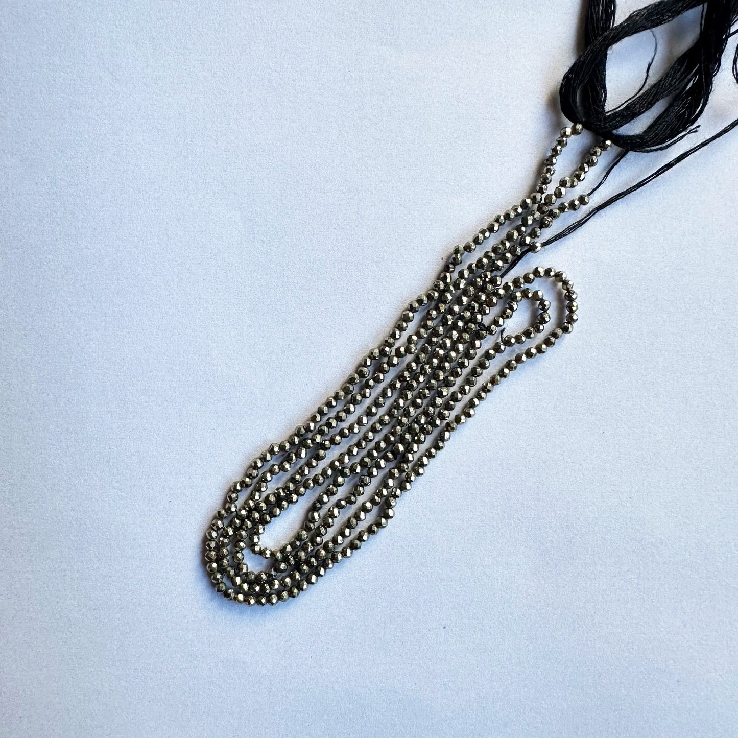 A jewellery artisan arranges Pyrite beads, crafting a sophisticated gemstone design.