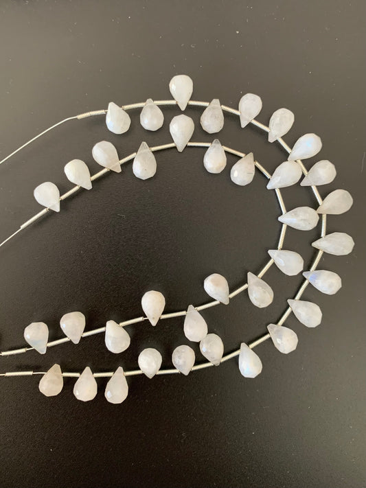 Beautiful strands of white moonstone beads lies on a dark surface, emphasising their subtle lustre and elegance.