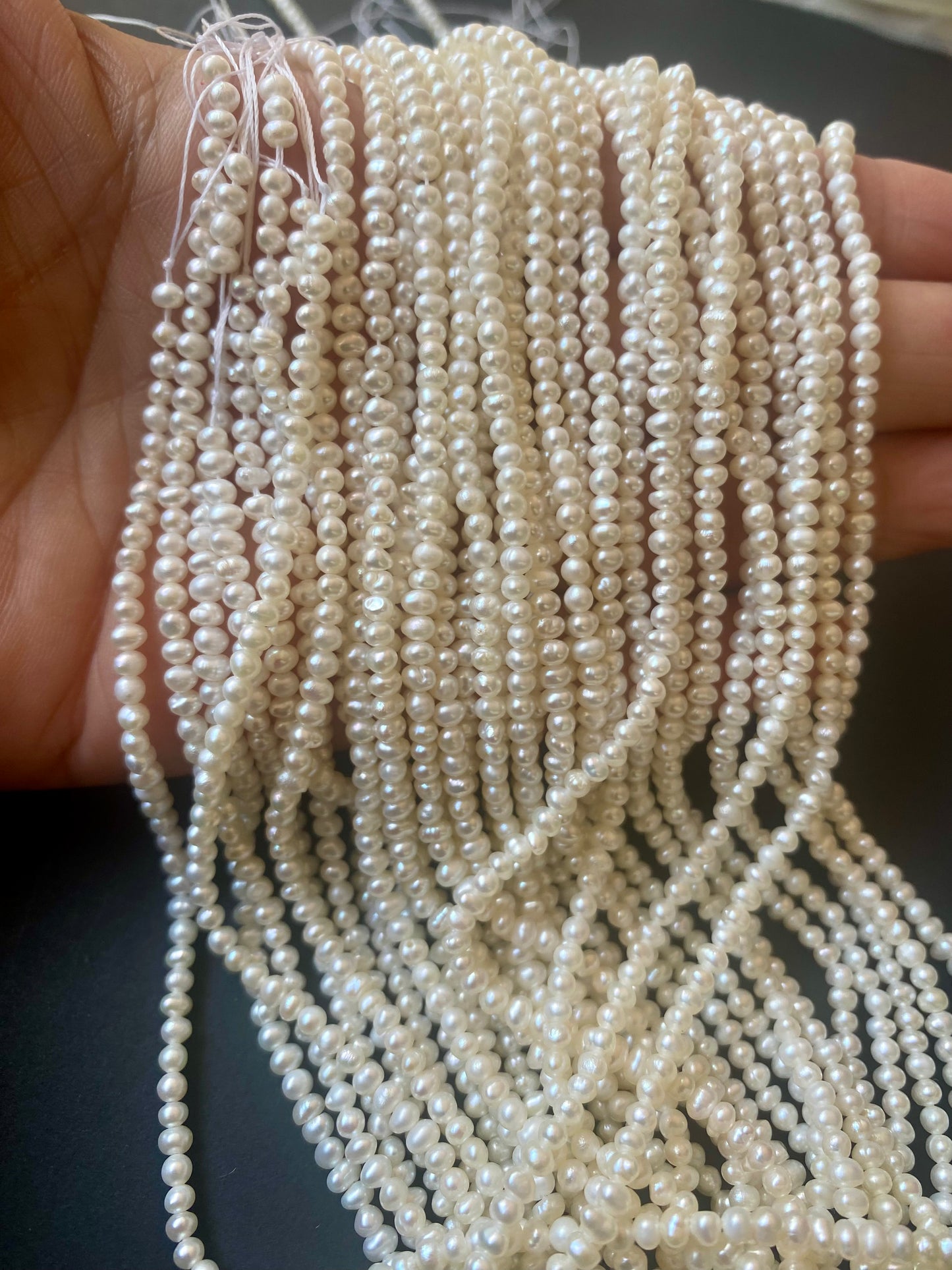 A person holding a strand of Rondelle Freshwater Pearls, showcasing their elegant white lustre and smooth texture.