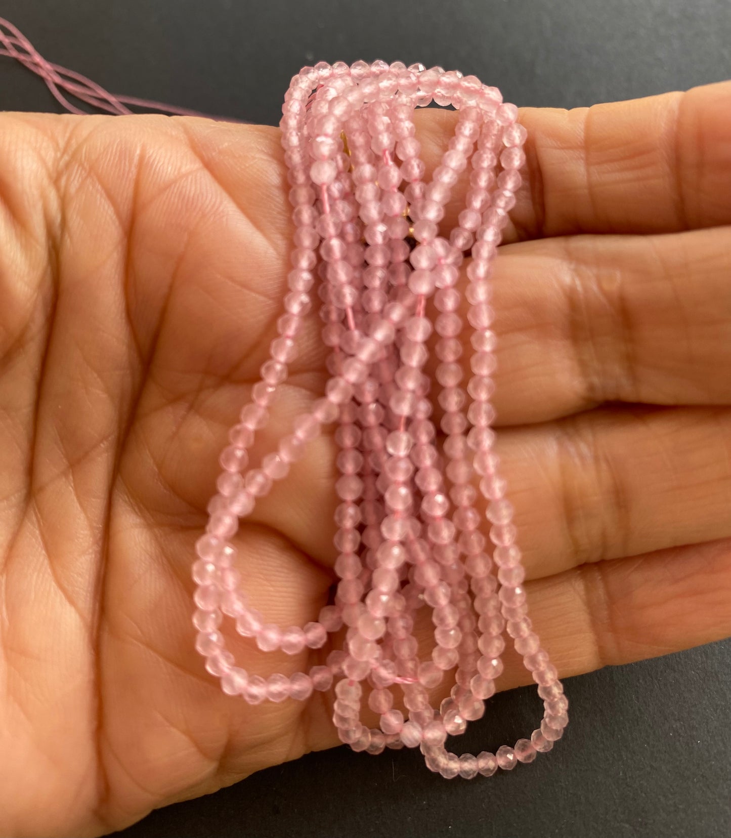 Close-up of a person holding a stunning pinkish Rose Quartz gemstone strand, highlighting its intricate facets.