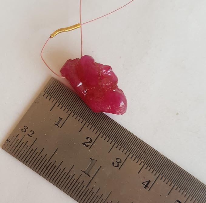 Close-up of a measuring ruler beside colourful precious bead, ruby.