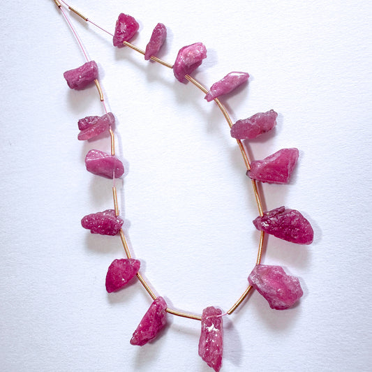 Close-up of 68 carats of ruby beads with raw finish and side drill, arranged in a loose cluster.