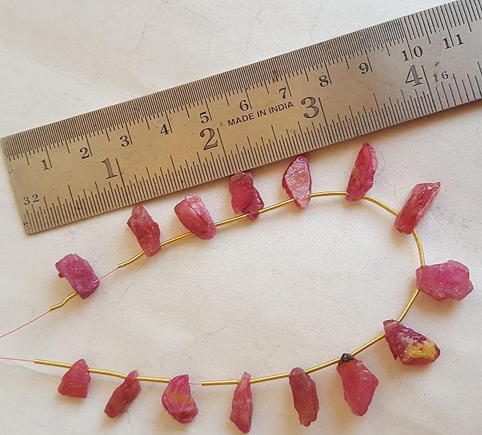 A ruler beside a cluster of pinkish red ruby gemstone beads.