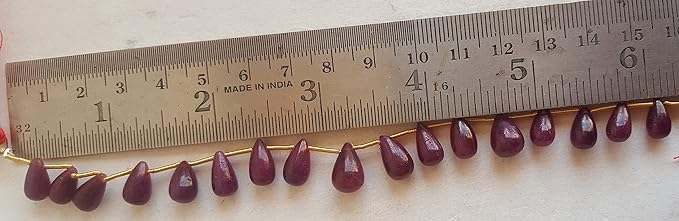 Close-up of a measuring rulers beside colourful precious beads, ruby tear drop shaped gemstone beads.