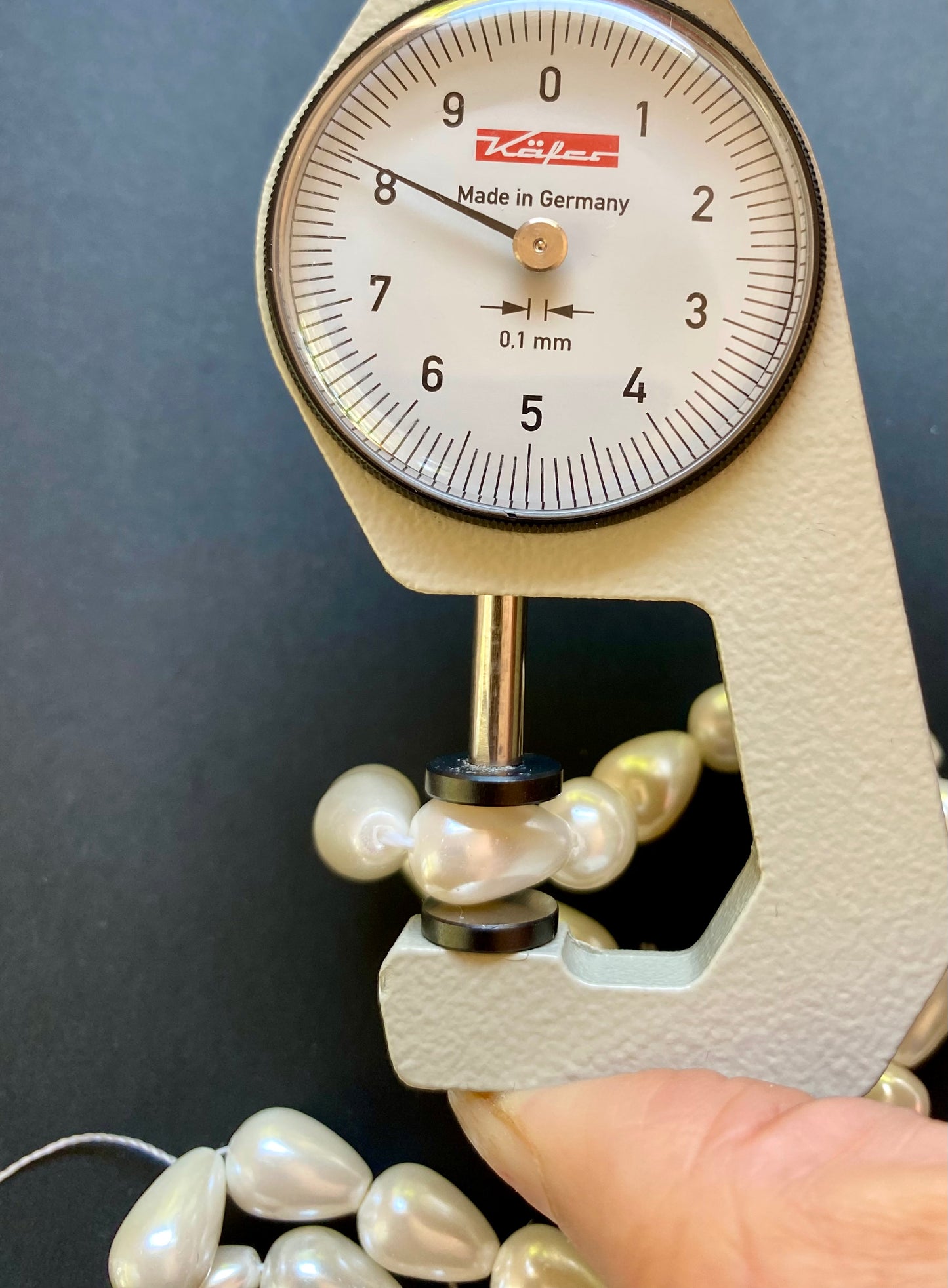 A person uses a measuring dial gauge to measure an elegant necklace of 8-12mm cone freshwater pearls, highlighting its measurement