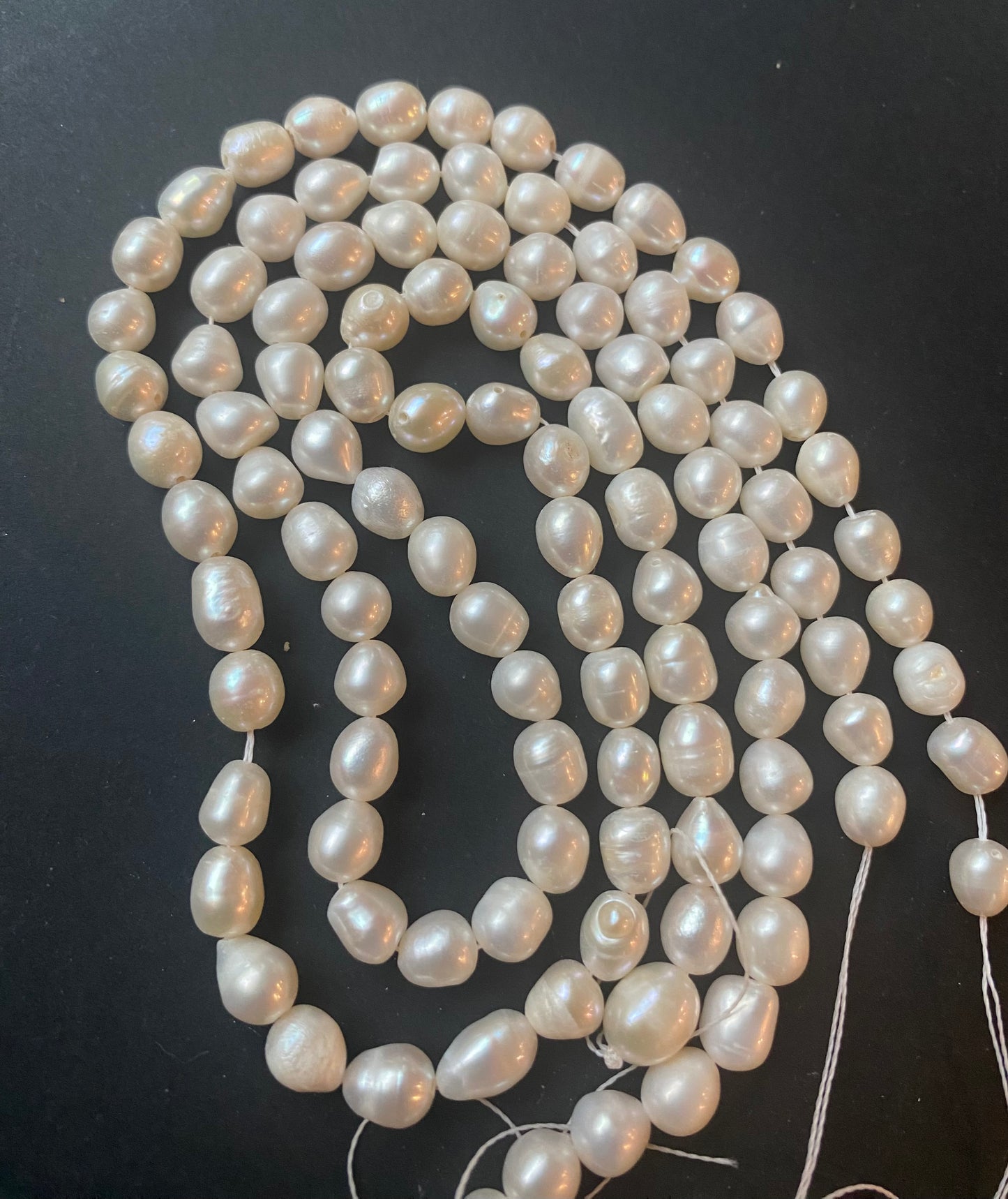 A beautiful strand of 6.5mm freshwater smooth baroque pearl beads resting on a sleek black background, showcasing their lustre.