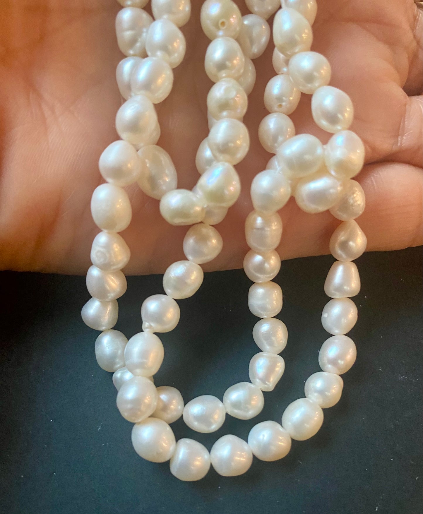 A hand grips a beautiful strand of 6.5mm freshwater pearls, highlighting their smooth texture and shine.