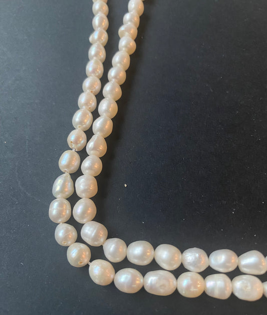 A strand of lustrous 6.5mm freshwater baroque pearl beads laid out on a dark black surface, highlighting their elegance.